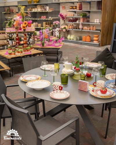 Table ronde de jardin grise et chaises assorties, dressées avec de la vaisselle colorée dans un magasin de décoration.
